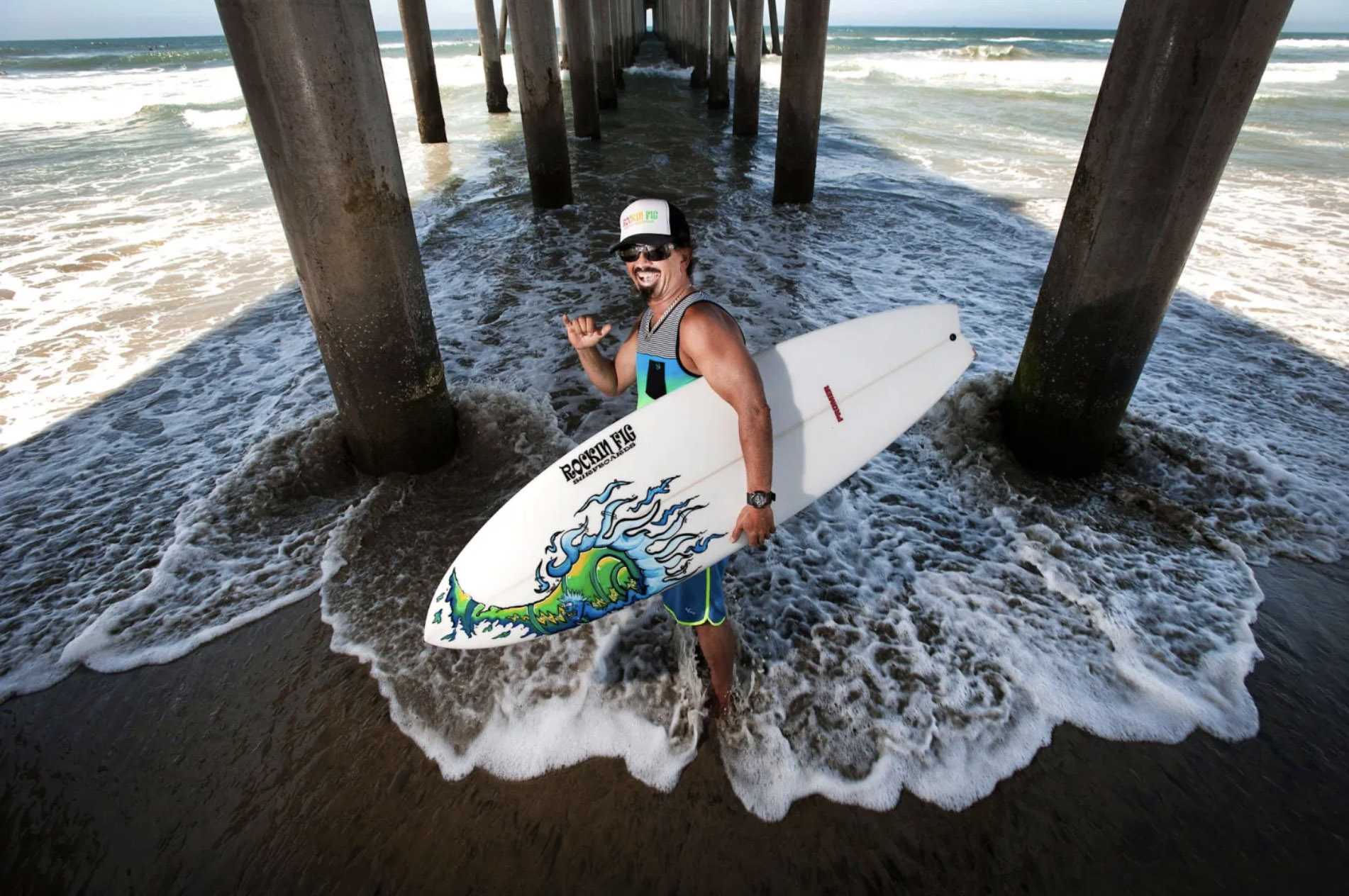 Rick “Rockin Fig” Fignetti stands with his surfboard under the Huntington Beach Pier on July 16, 2013. (Photo by Ed Crisostomo, Orange County Register/SCNG)